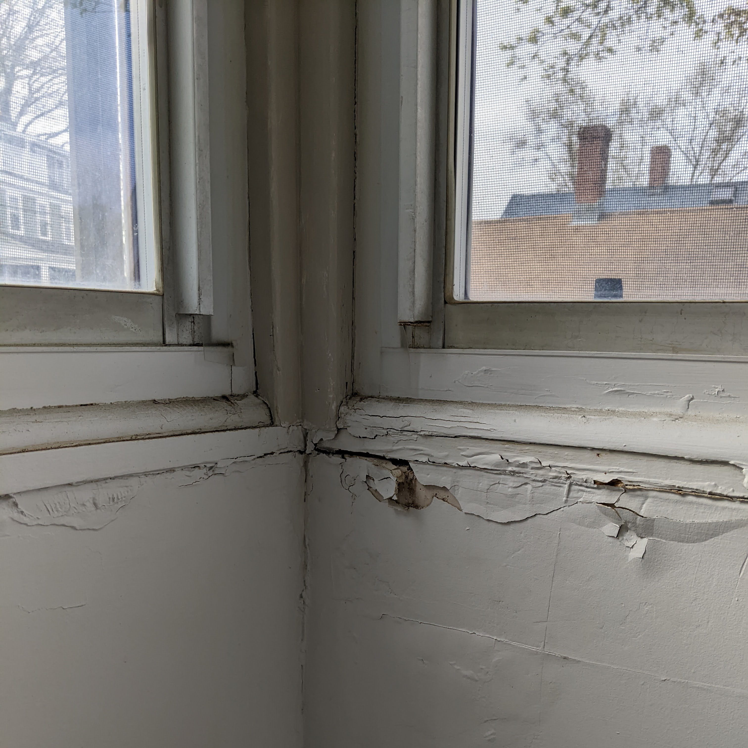 Close-up view of a damaged window corner showing peeling paint and cracks in the wall, indicating potential foundation issues.
