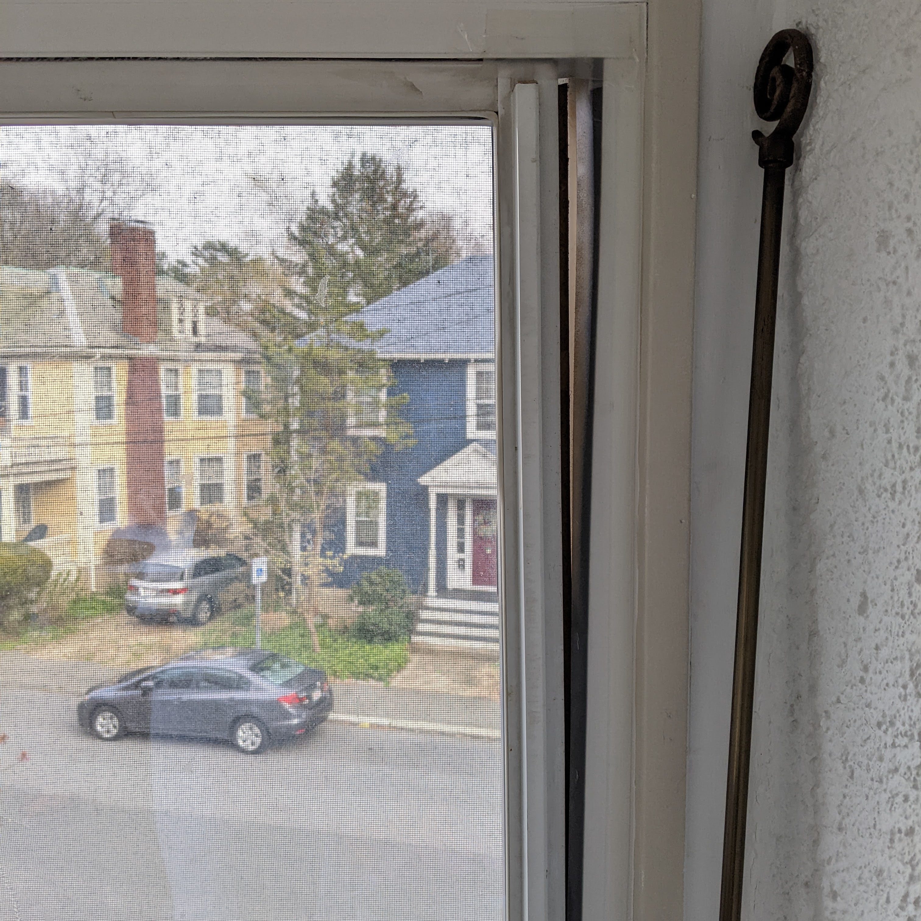 View of the exterior of a two-family house in Salem, Massachusetts, through a window screen, showing a parked car and surrounding neighborhood.