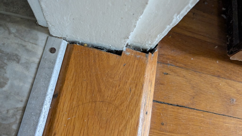 Close-up of a gap between the wall and wooden floor in a house, indicating possible foundation issues.